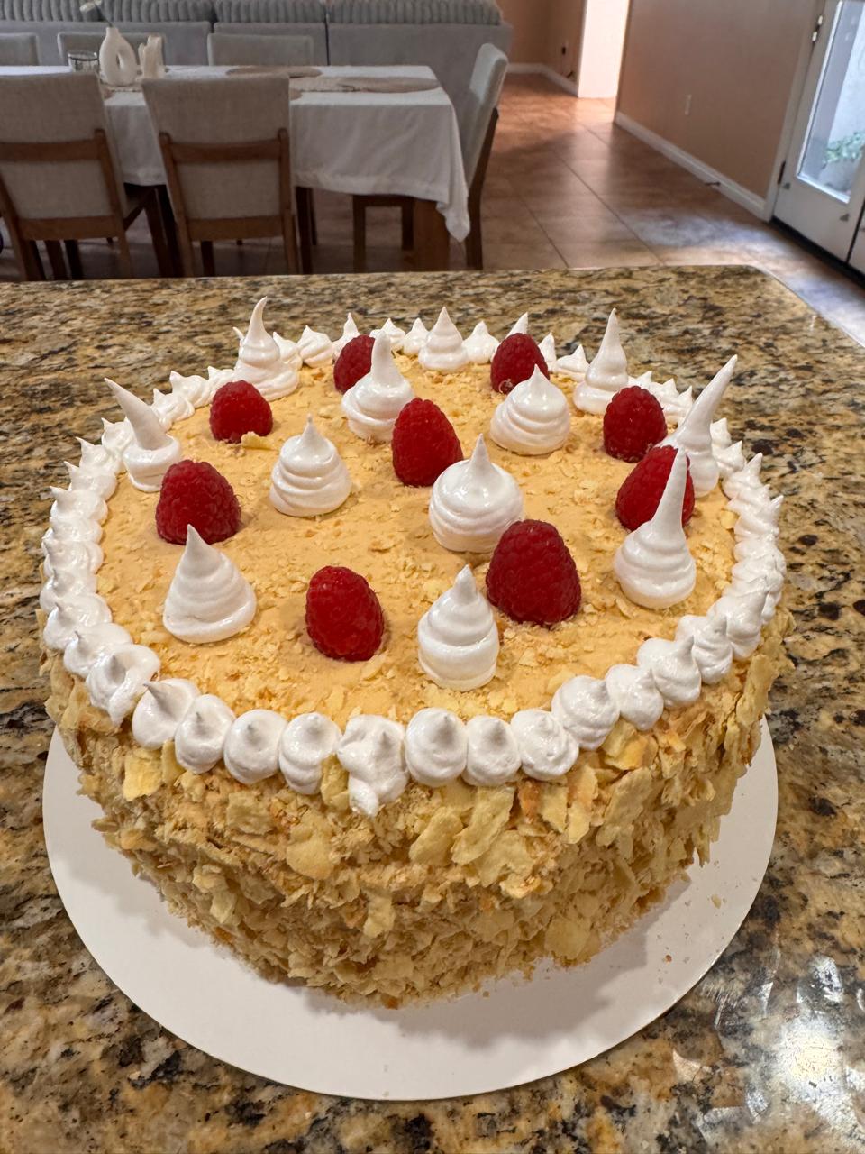 Torta Amor entera decorada con merengues y frambuesas frescas sobre los bordes de hojarasca